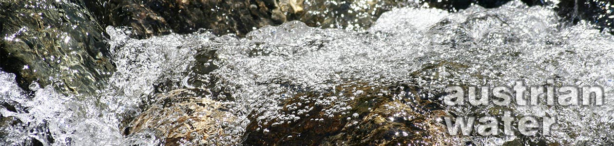 Sprudelndes Wasser fließt über Steine, die mit spritzenden Wassertropfen bedeckt sind, im Hintergrund Text 